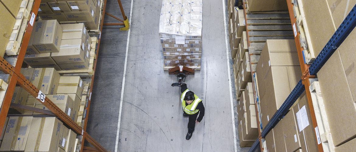 Mann i et lagerlokale med en jekketralle med mange boksesr pakket  og merket for utkjøring