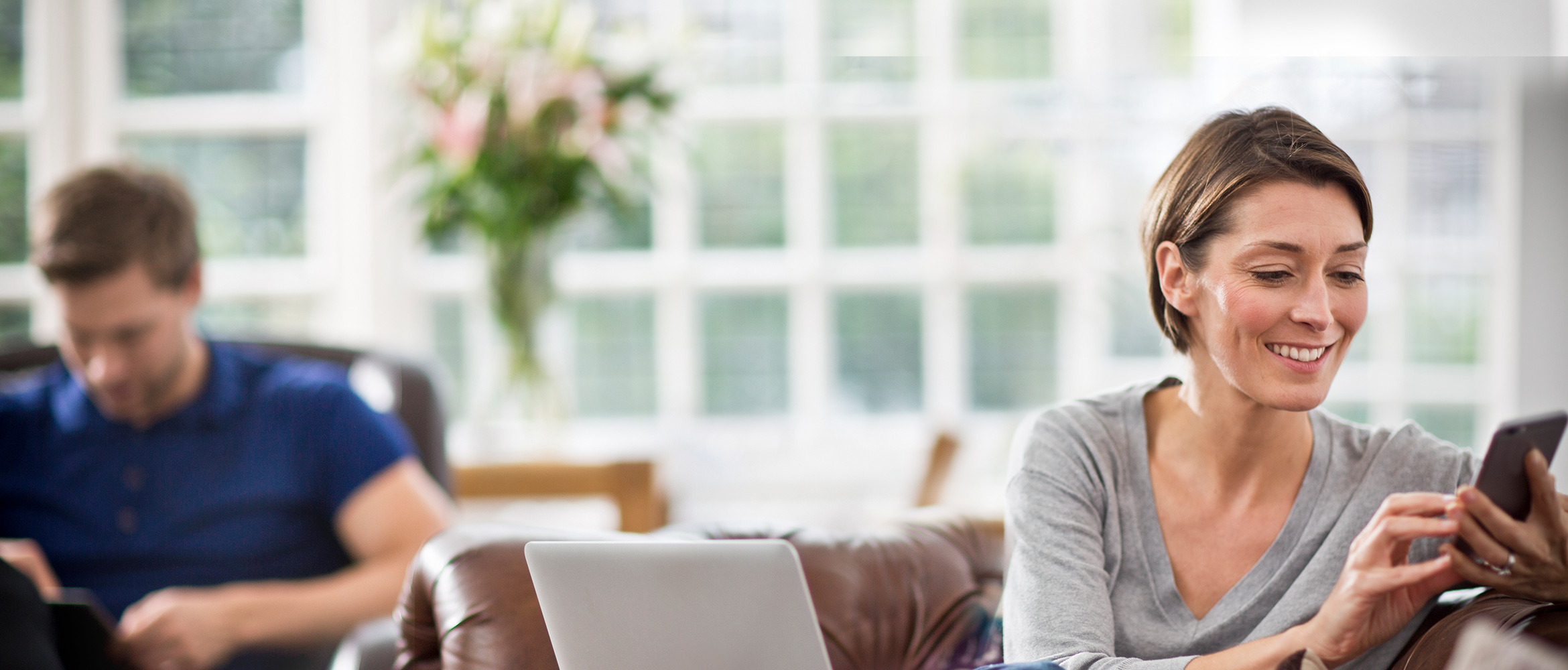 woman sat on sofa working on her phone and laptop