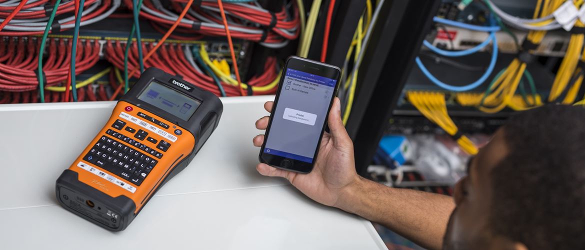 Network technician holding a smartphone and using the free Brother iLink&Label app to transfer cable IDs to the Brother PT-E550WNIVP label printer