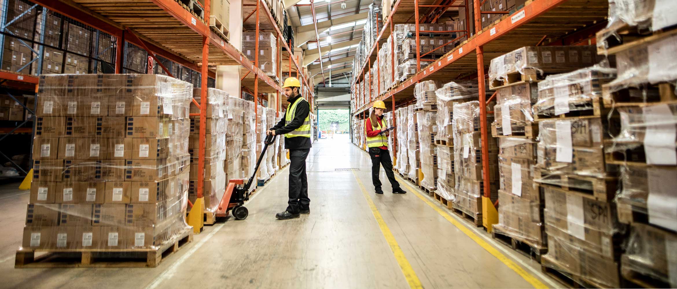 Man and woman working in warehouse, pump truck, pallets, orange racking