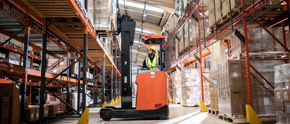 Man driving orange fork lift moving pallet from racking in warehouse and distribution centre