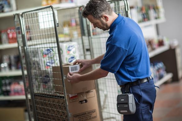 Warehouse worker applying a barcode label onto a brown box, that has been printed on the Brother RJ portable printer