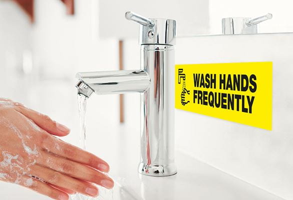 Person som vasker hender og det spruter vann på et informasjonsskilt om håndvask