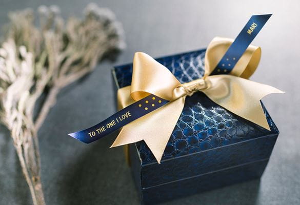 Gift box wrapped with a generic yellow ribbon, and Brother gold on blue satin ribbon with printed message