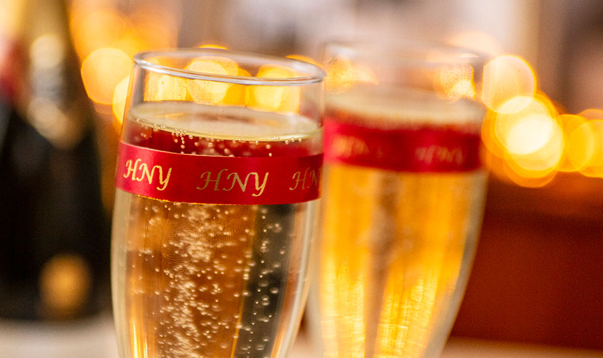 To champagneglass pyntet med et rødt Brother silkebånd med teksten HNY (godt nytt år)