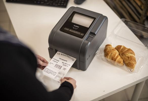 Close up a Brother label printer printing out a food day label for a pack of croissants in the back office of a food deli, bakery or cafe