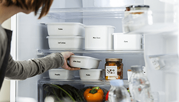 En kvinne setter inn en boks med mat i et kjøleskap med bokser som er merket med Brother P-touch merketape