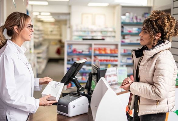 Female pharmacist with glasses at counter service female customer with curly hair wearing coat