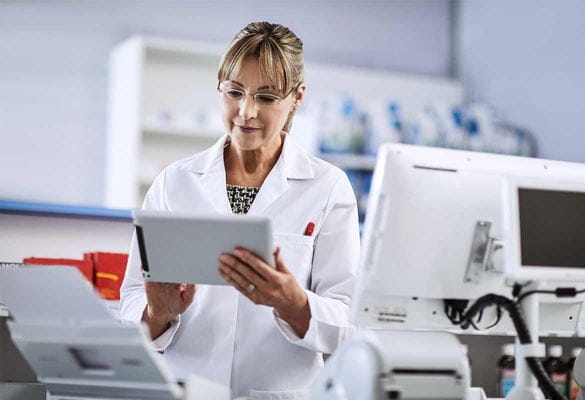 Female pharmacist wearing white coat using tablet device