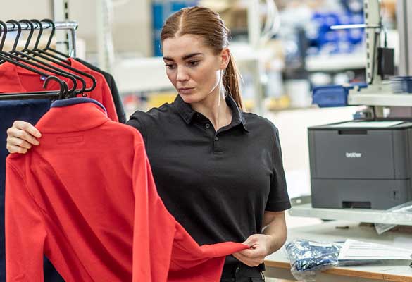 Female wearing black holding red fleece, table, printer in fulfilment centre and sortation