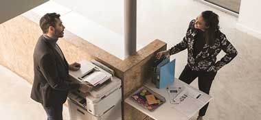 Aerial view of man and woman stood around a Brother printer