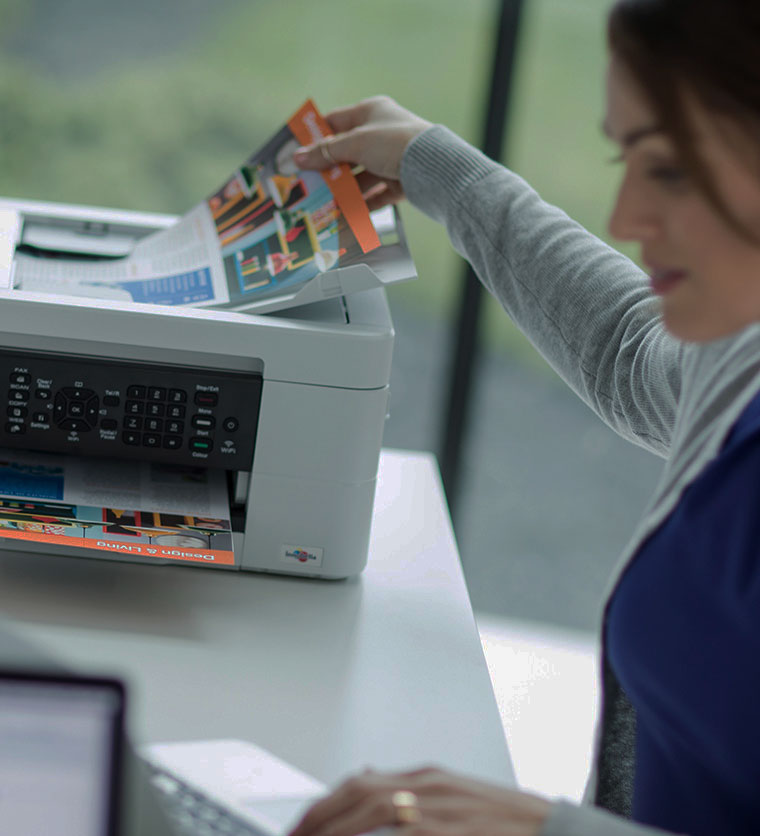 En kvinne sitter ved et skrivebord og plasserer et dokument i dokumentmateren på en printer