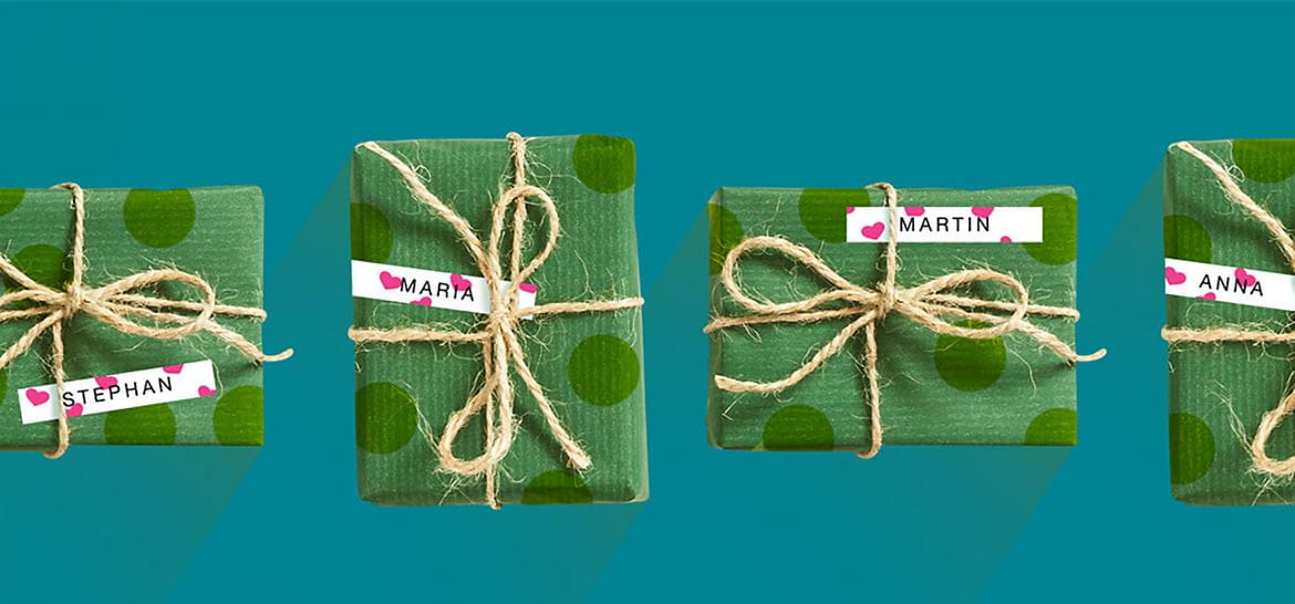 En rad med julegaver pakket inn i grønt papir merket med en hvit Brother P-touch merkelapp med rosa hjerter