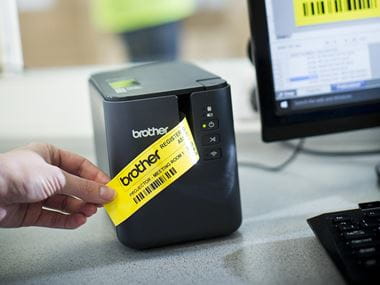 En person holder en gul etikett med sort skrift som er skrevet ut på en Brother PTP900W merkemaskin