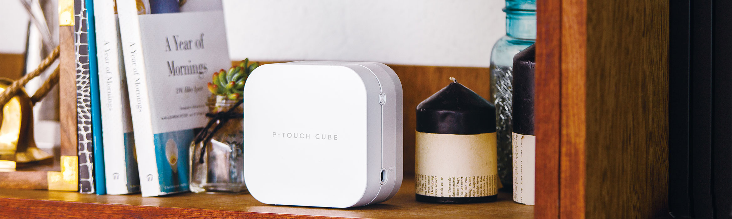 Brother P-touch CUBE merkemaskin for utskrift av merkelapper og silkebånd står i en hylle sammen med bøker, stearinlys og pynteting