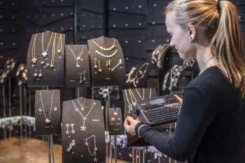 En ansatt hos Kalevala Koru skriver ut merkelapper på en P-touch merkemaskin som festes på smykkestativ i butikken