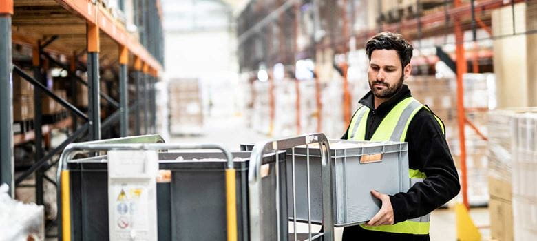 Man wearing hi-vis taking grey crate from cage in warehouse