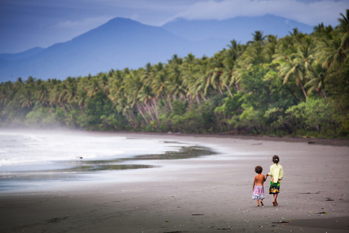Woman and child walking on a beach island surrounded by trees
