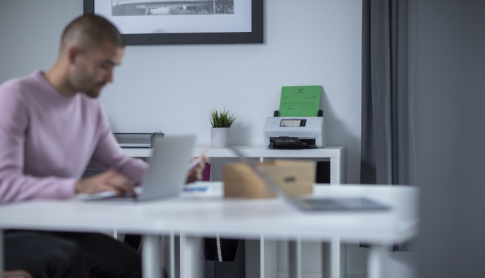 Mann som sitter å jobber på en pc med en skanner i bakgrunnen
