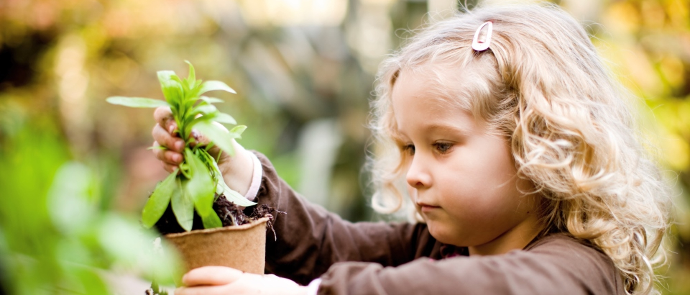 Niña de pelo rubio cogiendo una maceta y una planta