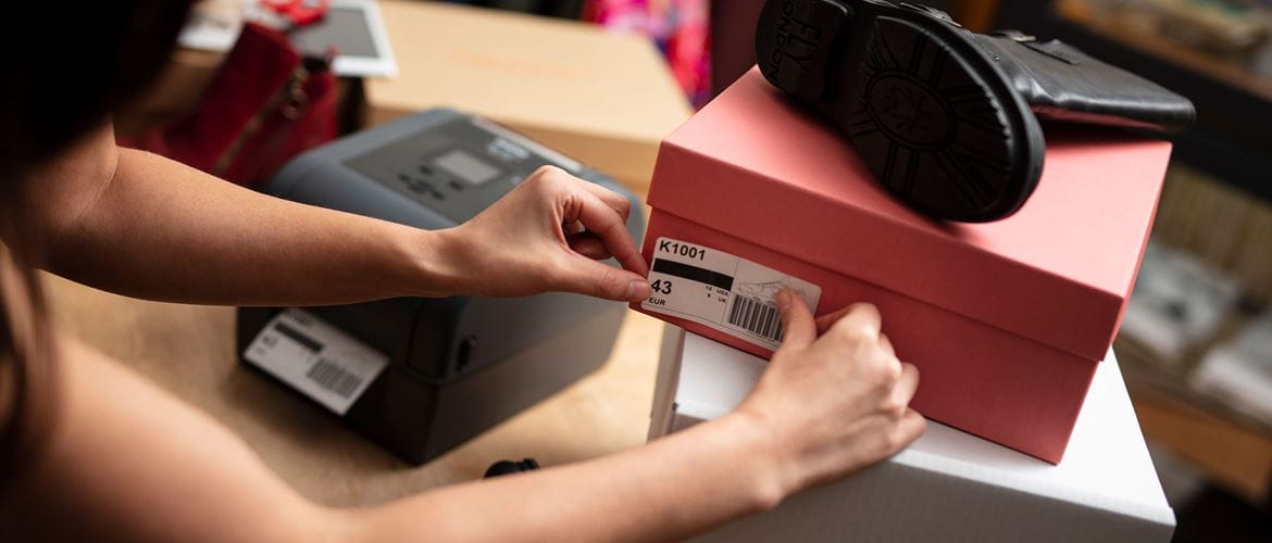 Lady sticking shoebox label onto a pink shoe box in front of Brother TD desktop label printer