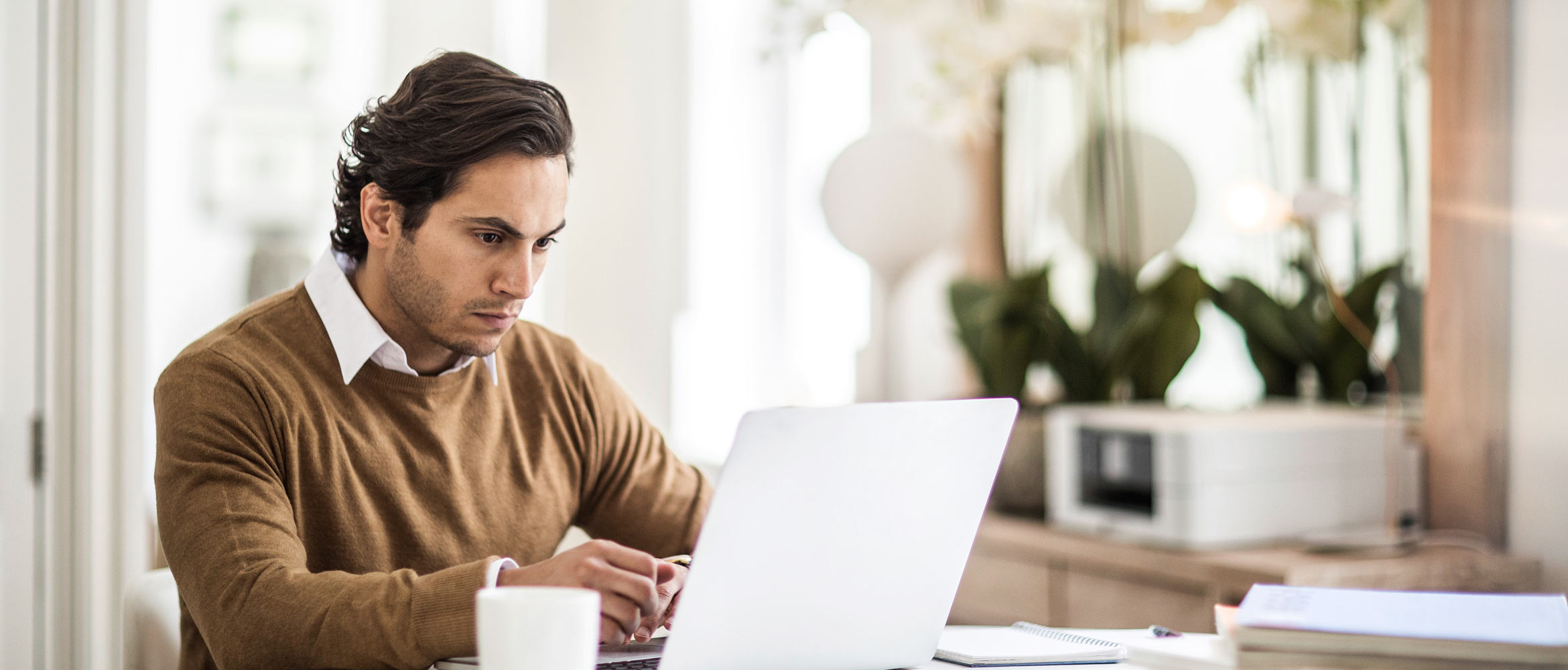 Homem com pulôver marrom usando laptop