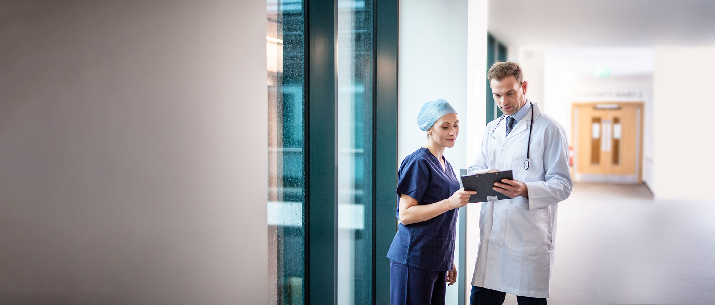 Male doctor in white coat and stethoscope with female doctor in corridor of hospital