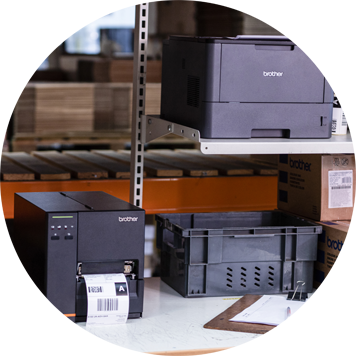 Dark grey Brother printer and label printer on bench, clipboard, paper, racking, boxes