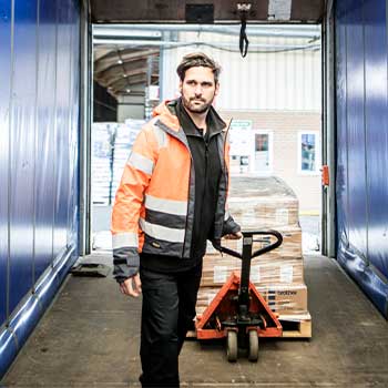 Man wearing orange hi-vis coat pulling pump truck with boxes in truck with blue sides