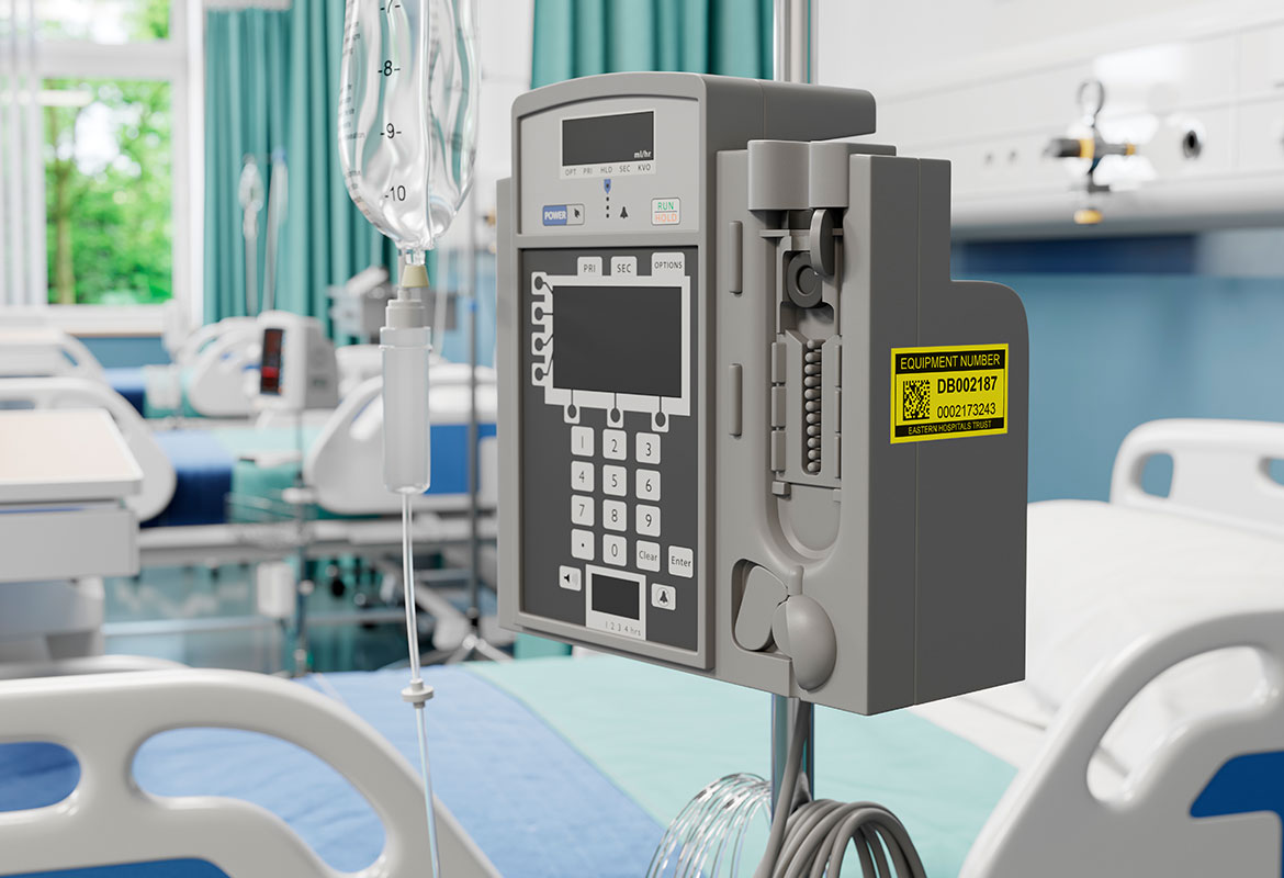 Yellow maintenance label on side of IV infusion pump in hospital ward next to bed