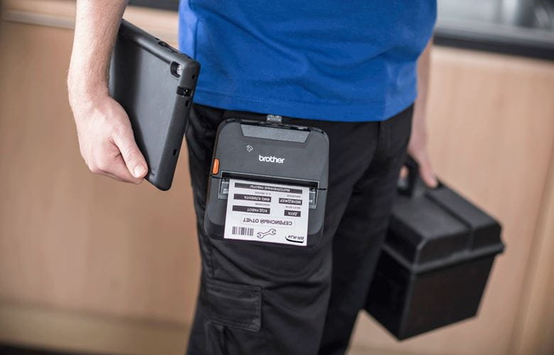 Workman in blue t-shirt holding workbox and tablet with rj printer on belt clip printing