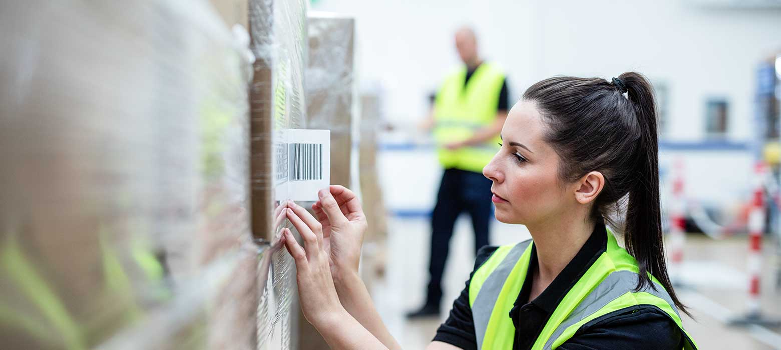 Female with hi-vis putting barcode label on to pallet of boxes in fulfilment centre