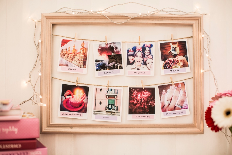Wooden frame with lights around it and 8 photos inside that are pegged onto string