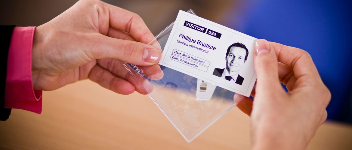 Close-up of a woman inserting a visitor ID printout into a clear clip-on badge