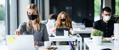 Four colleagues in an office environment working at desks that are spaced apart while wearing face masks to comply with covid-19 guidelines