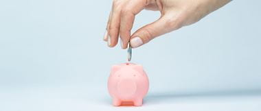 hand places coin into tiny piggy bank