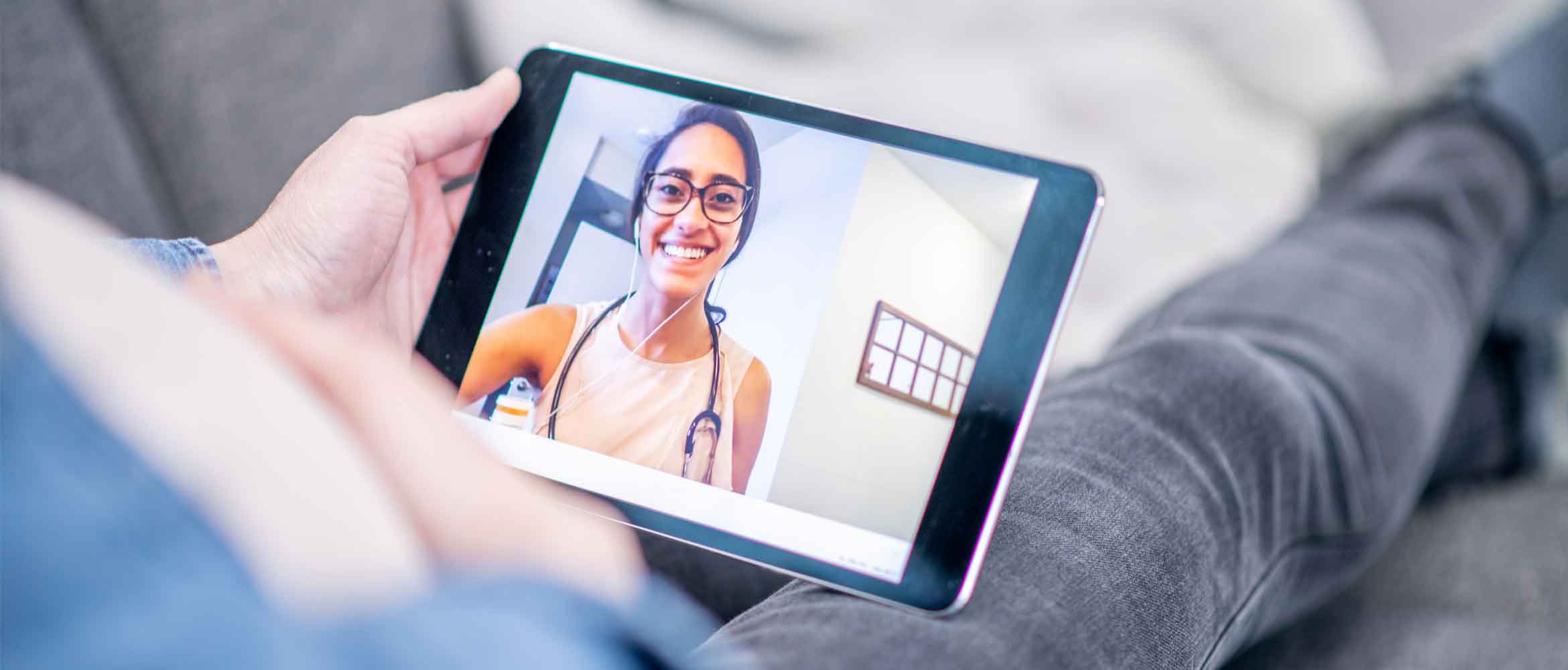 A patient at home on the sofa having a conversation with a doctor on a tablet device