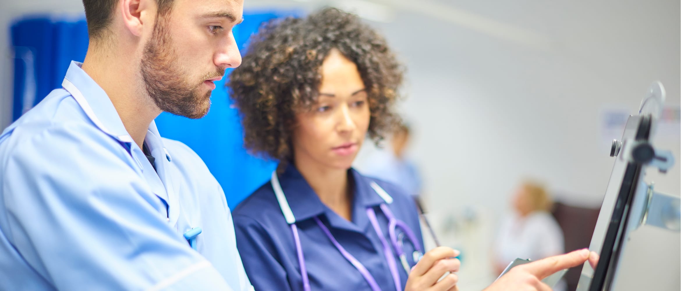 Male nurse checking information on a tablet device while being supervised by a female staff nurse