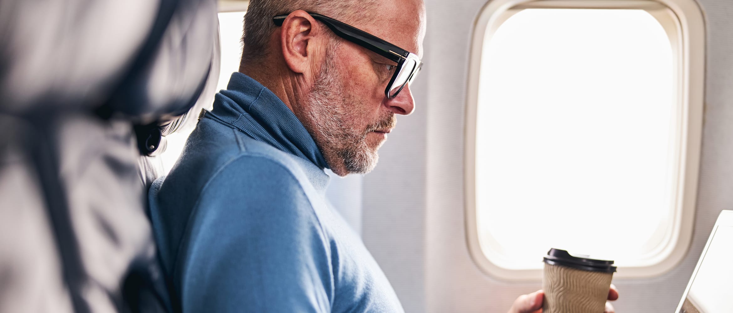 Man on an aeroplane who is working on his laptop whilst drinking a coffee