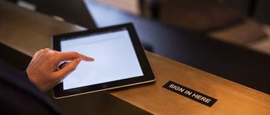 Close-up of a person using a tablet device to sign in at a reception desk