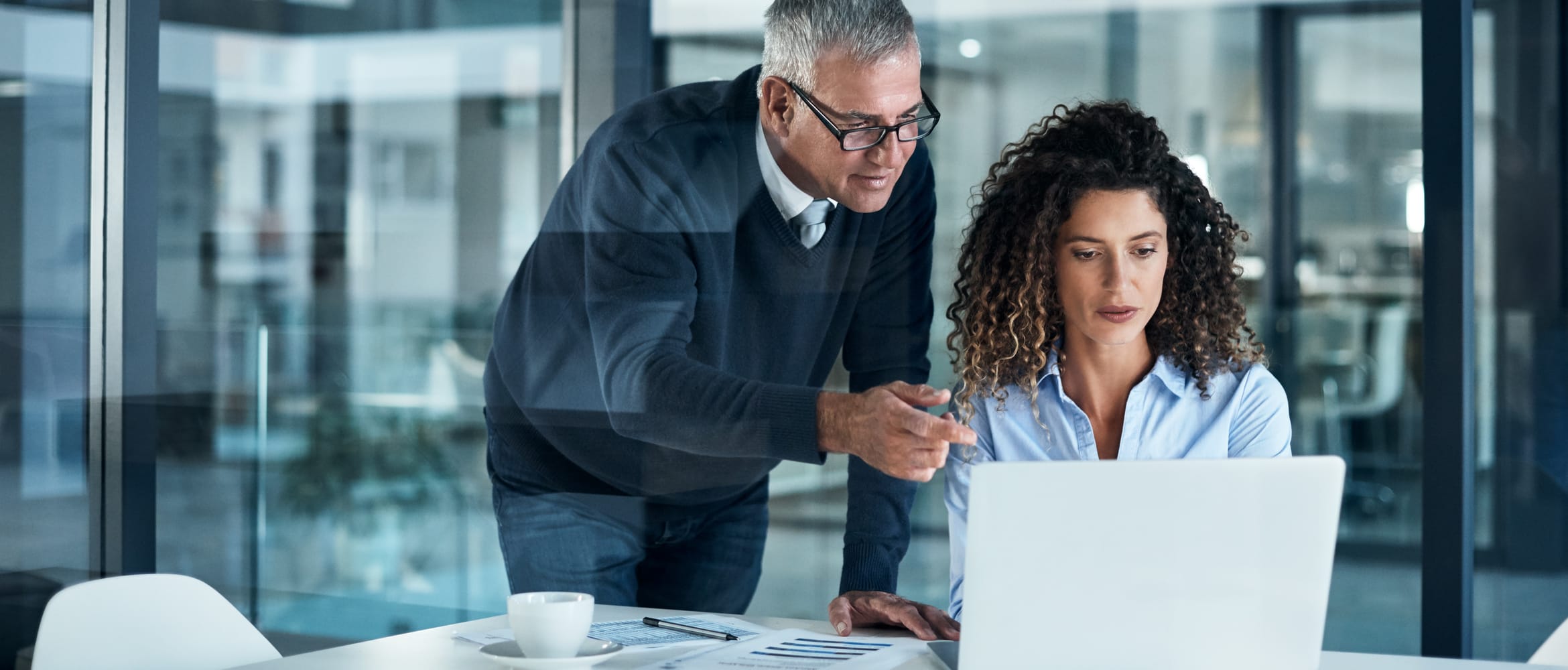 Business man and business woman working late on a laptop in a glass wall partitioned office