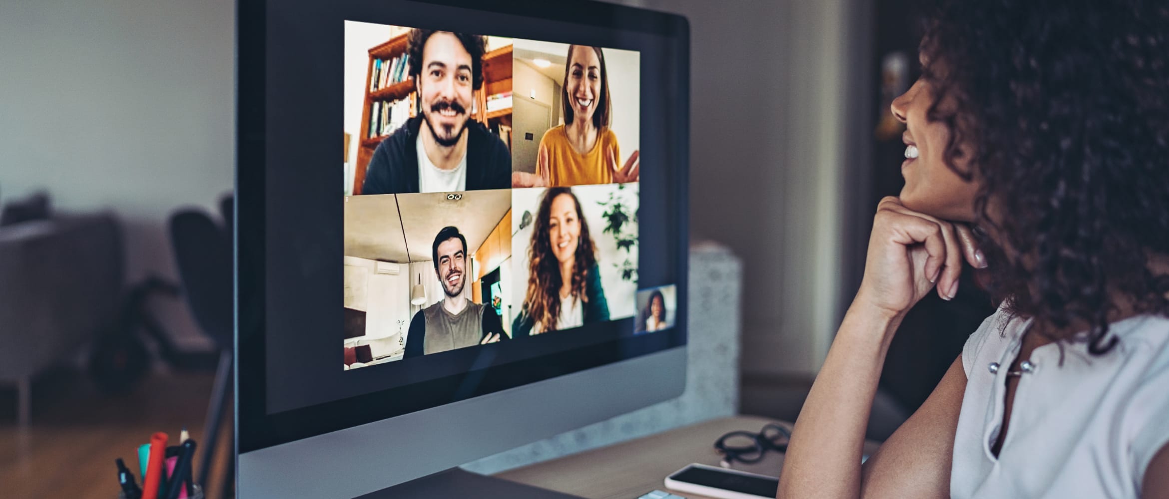 A woman having a video conference with four colleagues on a desktop computer in a home office environment