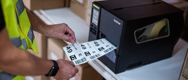 Close-up of a warehouse worker peeling a barcode label off a reel which is being printed from a Brother TJ industrial label printer