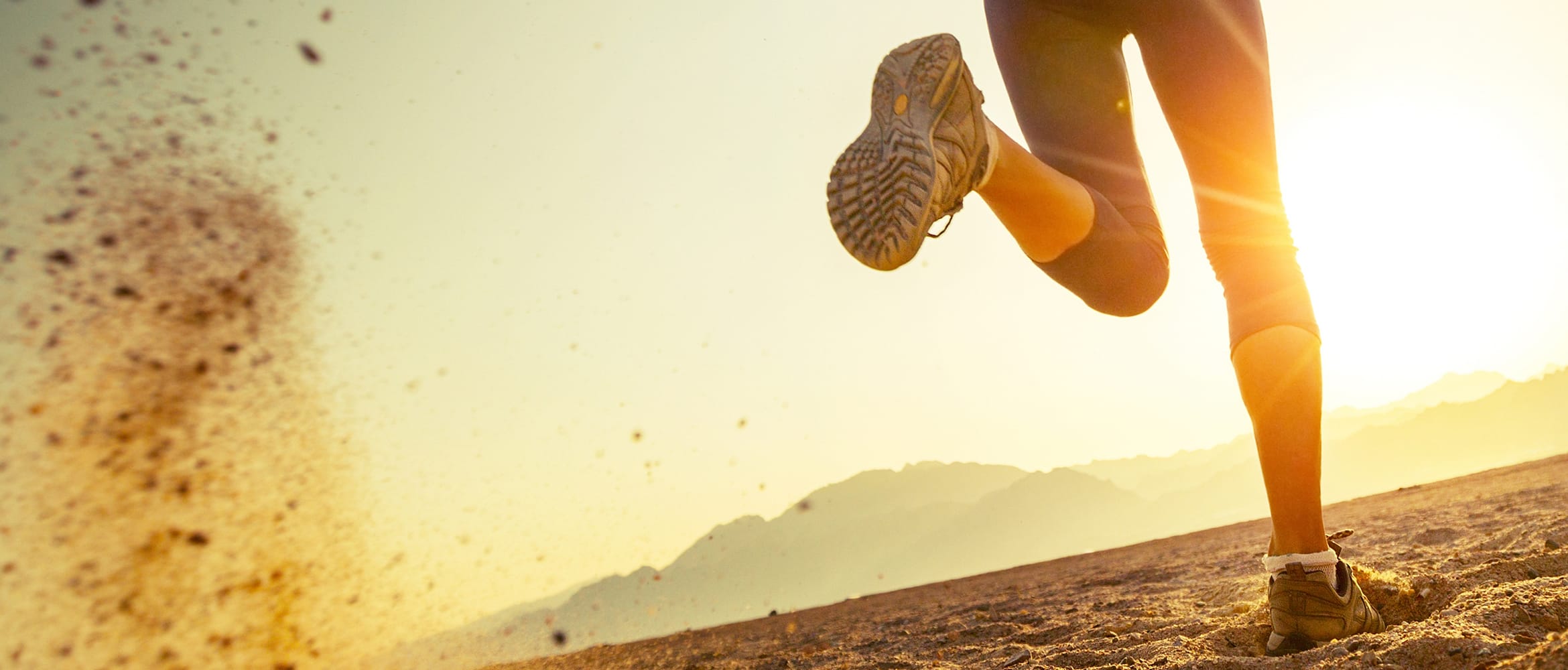 Woman kicks up dirt as she runs towards the sun