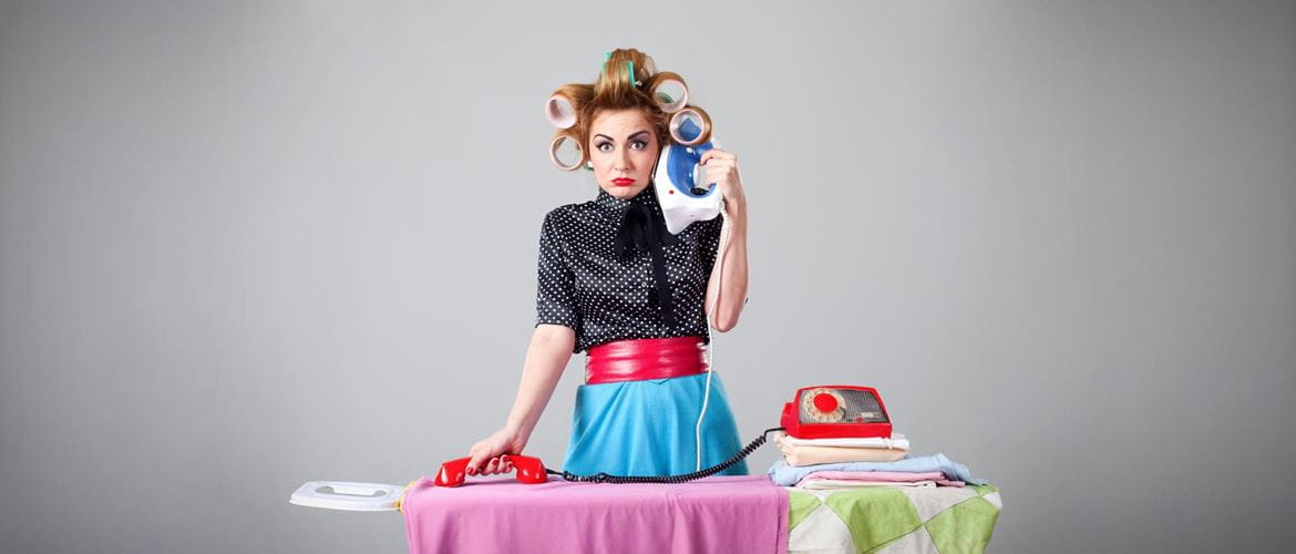 Multitasking woman puts an iron to her ear and irons a shirt with a phone to illustrate being overwhelmed