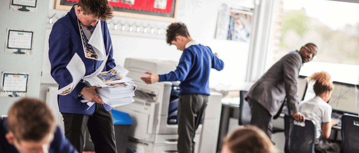 teacher looks on in dismay as students print hundreds of sheets of paper from classroom printer