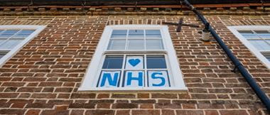 Vertical view of a home-made Love NHS sign attached to a sash window of a town house