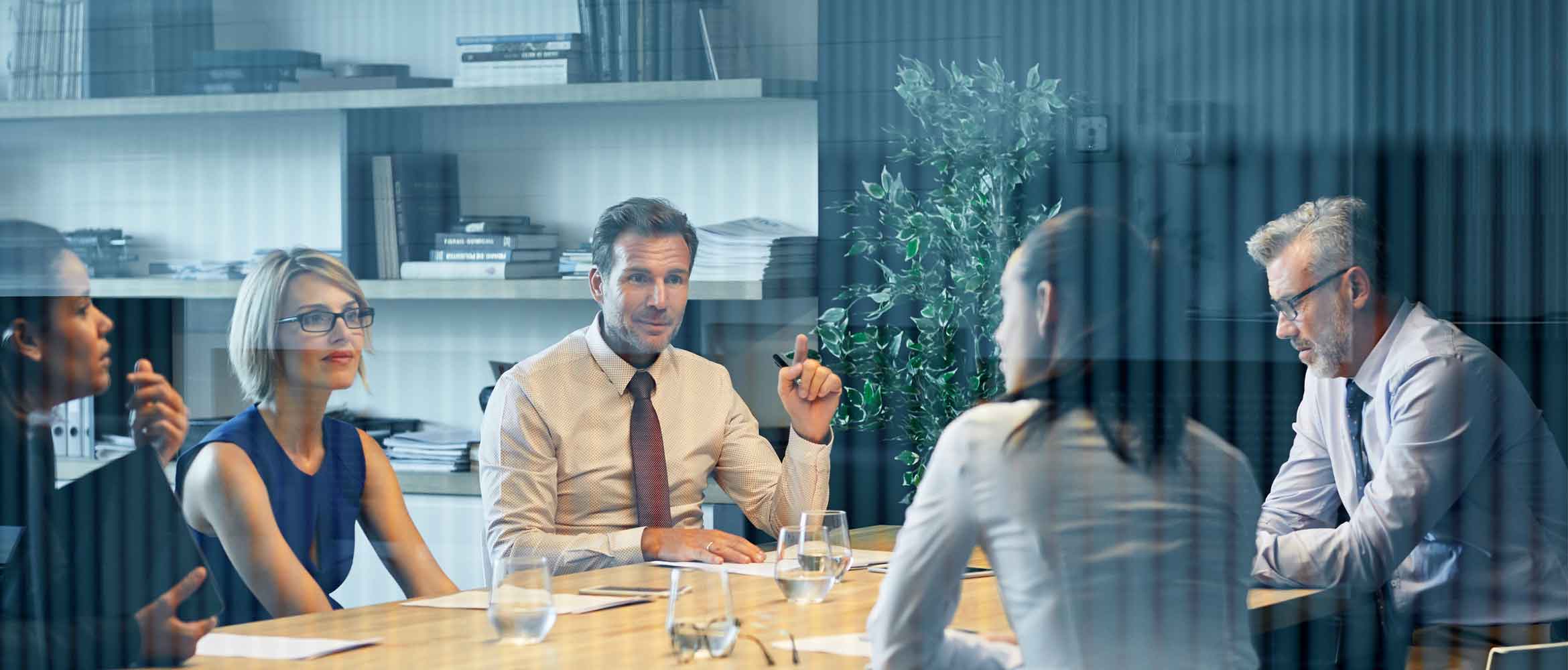 Business people communicating at desk seen through glass. Coworkers are discussing in meeting. They are sitting in office.