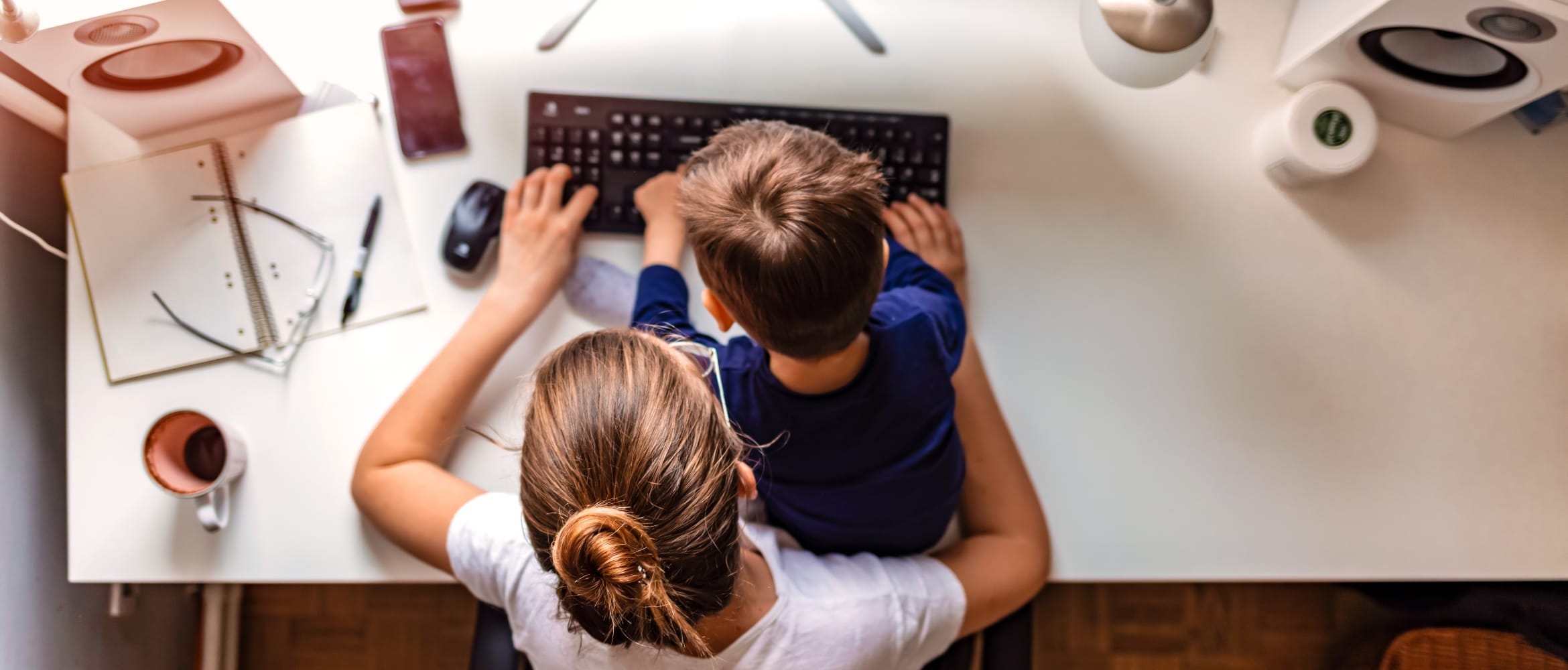 Overhead view of a young mother working on a desktop computer with her son sitting in her lap in a home office environment