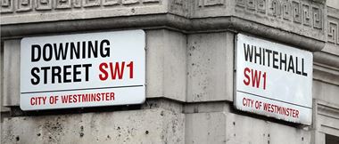 Close-up of Downing Street and Whitehall signs on the corner of a stone building where both streets meet in London
